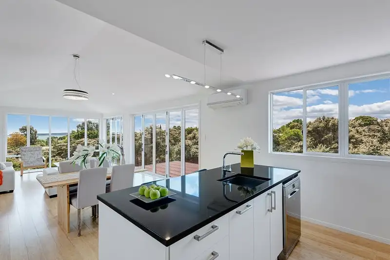 The open plan kitchen and dining room, a black benchtop island, timber floors and windows onto the bush and the sea.