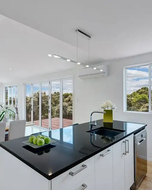 The kitchen in the new Maraetai home, a black benchtop island under big windows onto the bush.