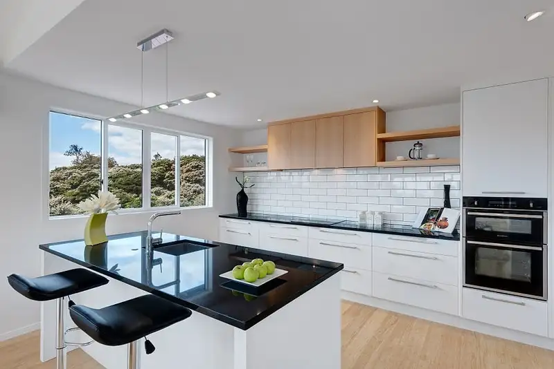 The kitchen island with its black benchtop, open timber shelves and a double wall oven.