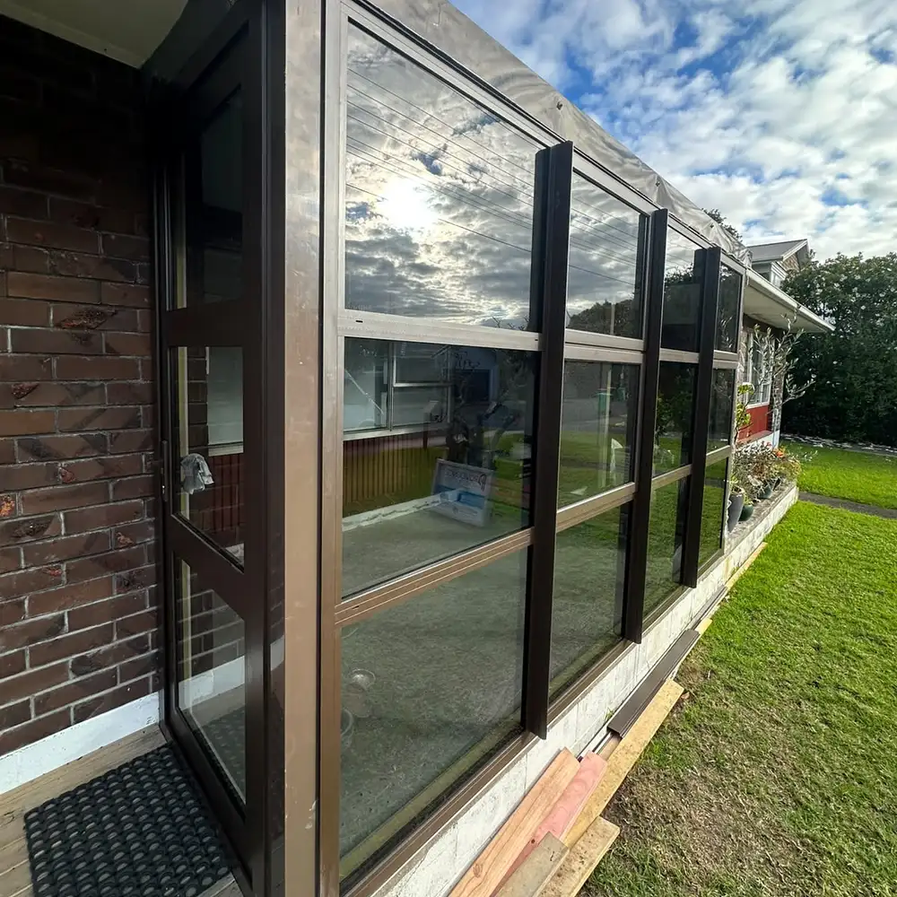 The finished conservatory from the side, the front porch closed in with dark framed glass and a glazed door.