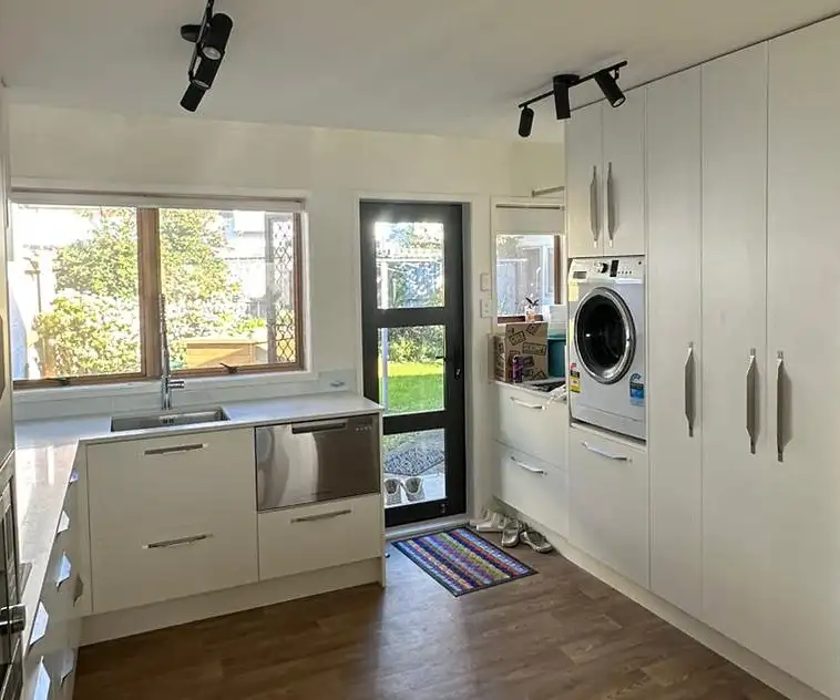 After: the finished kitchen and laundry, white cabinets with pull handles, black track lights, the new back door and the washing machine built in beside it.