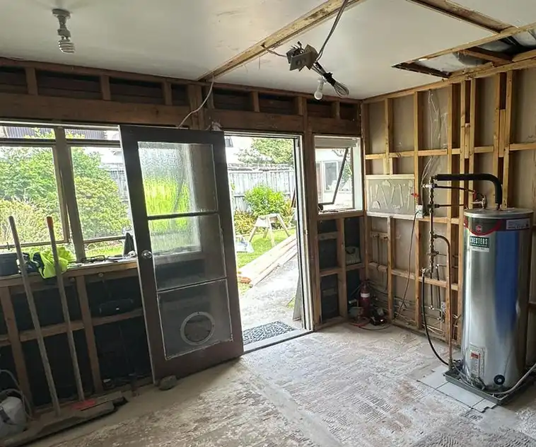 Before: the kitchen and laundry wall stripped to the framing, with the old back door and the hot water cylinder.
