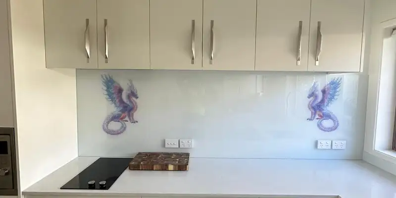 The finished hob wall, a glass splashback with a dragon at each end, between the white wall cabinets and the bench.