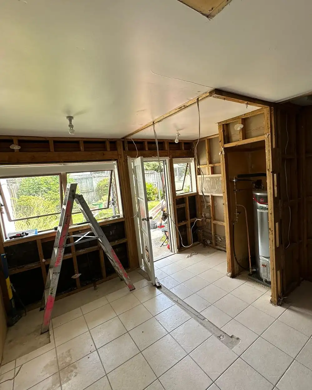 Before: the room stripped to the framing, the ceiling open, a ladder in the middle and the hot water cylinder in its alcove.